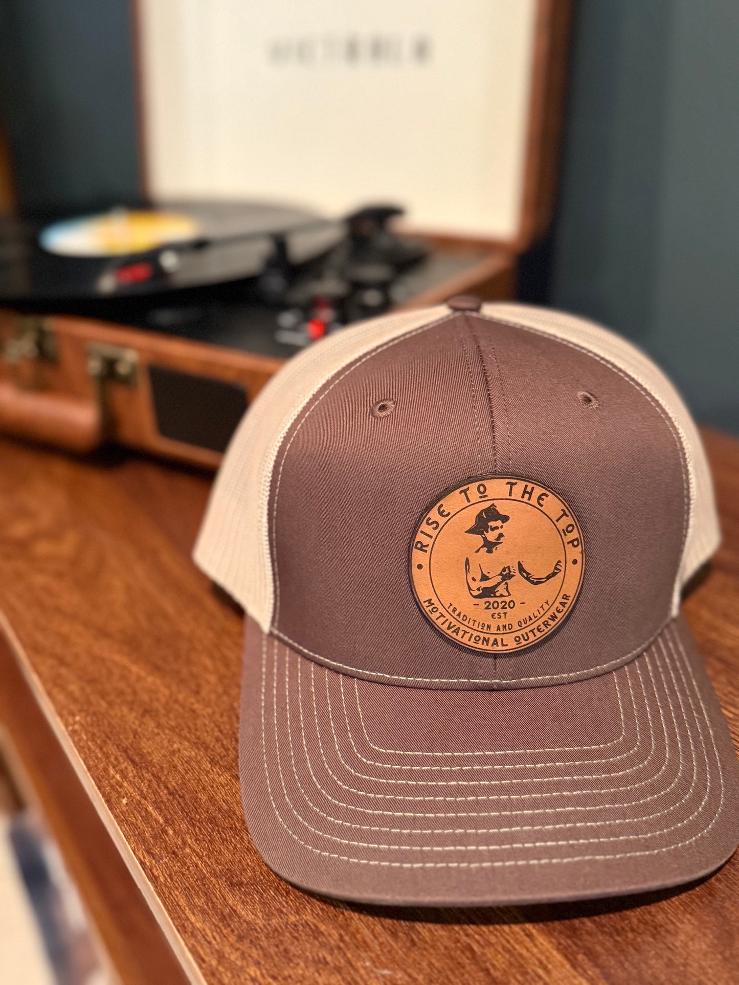 Brown and khaki trucker hat sitting on a wood looking surface in front of a record player.