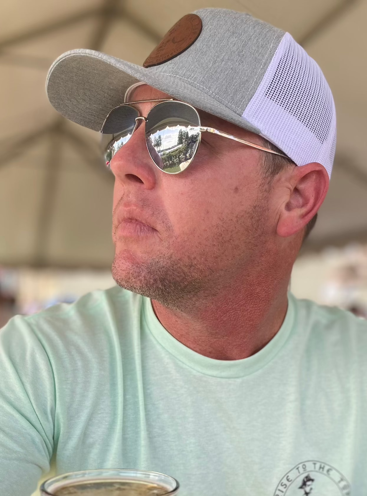 White man in sunglasses and mint green shirt wearing grey and white rise to the top trucker hat.