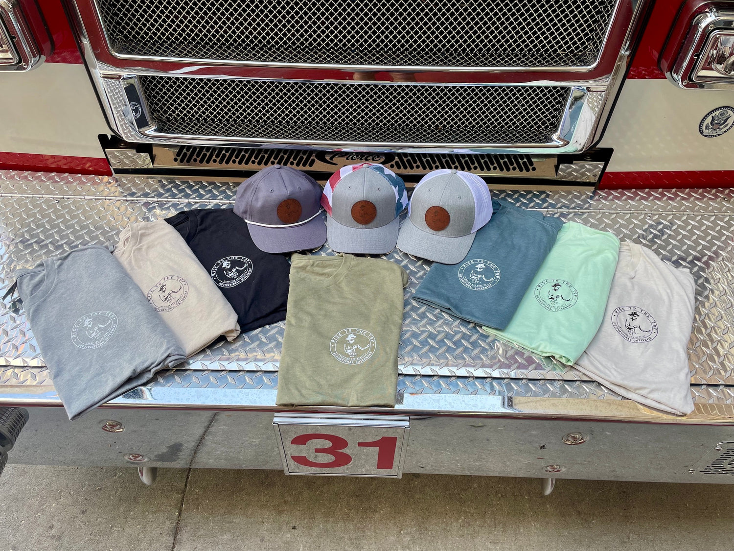 Seven rise to the top t-shirts and three hats laid out on a fire engine.