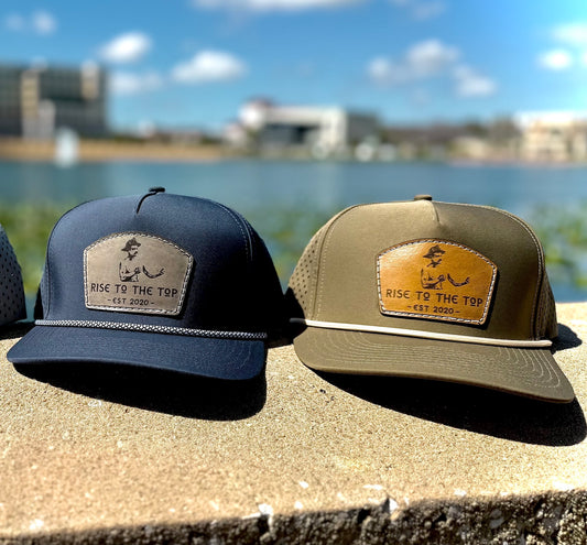 Two hats one navy one olive with a brand logo on a ledge by a body of water.