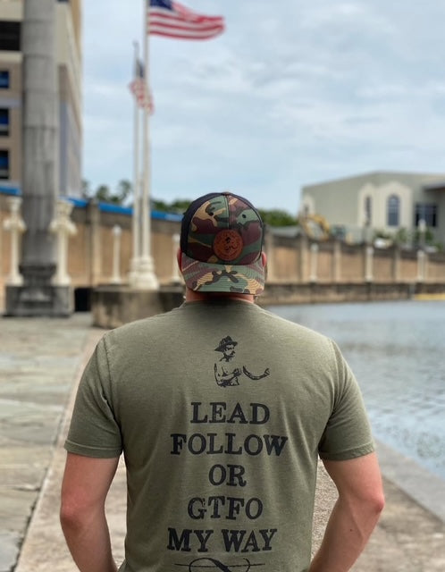 Back of military green T-shirt with logo in black and black writing underneath lead follow or GTFO my way