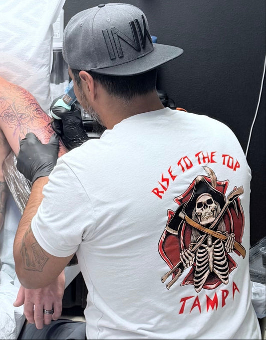 Tattoo artist working on a client's arm with tattoo supplies in the background.